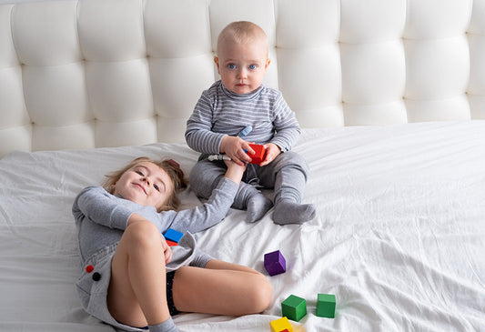 Baby and older sibling on bed holding hands